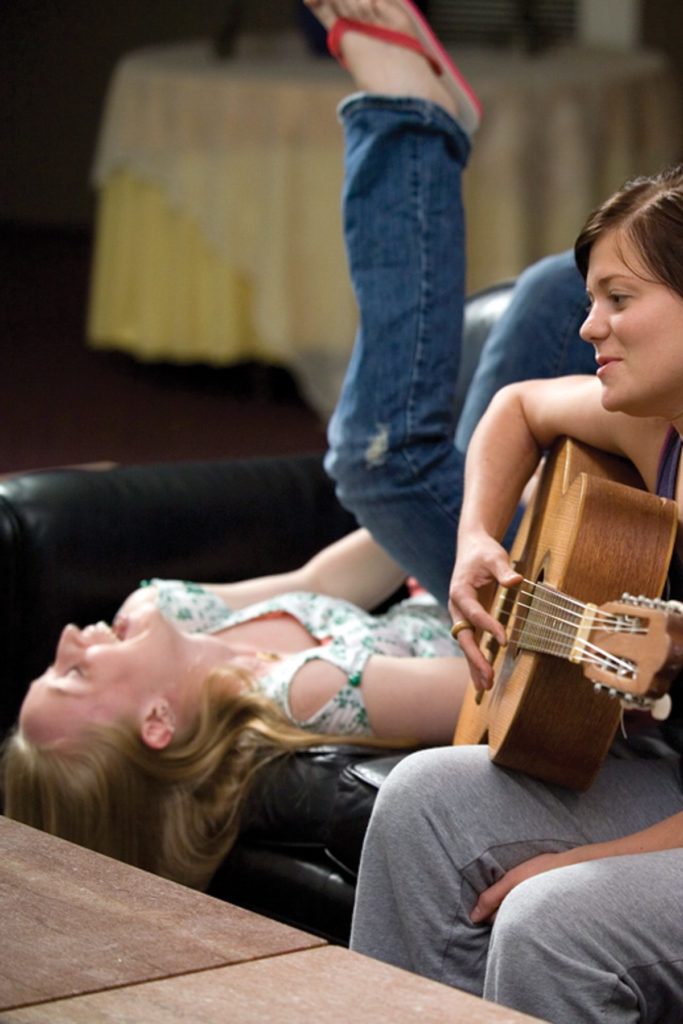 Two students laughing, singing, and playing guitar inside dorm common area