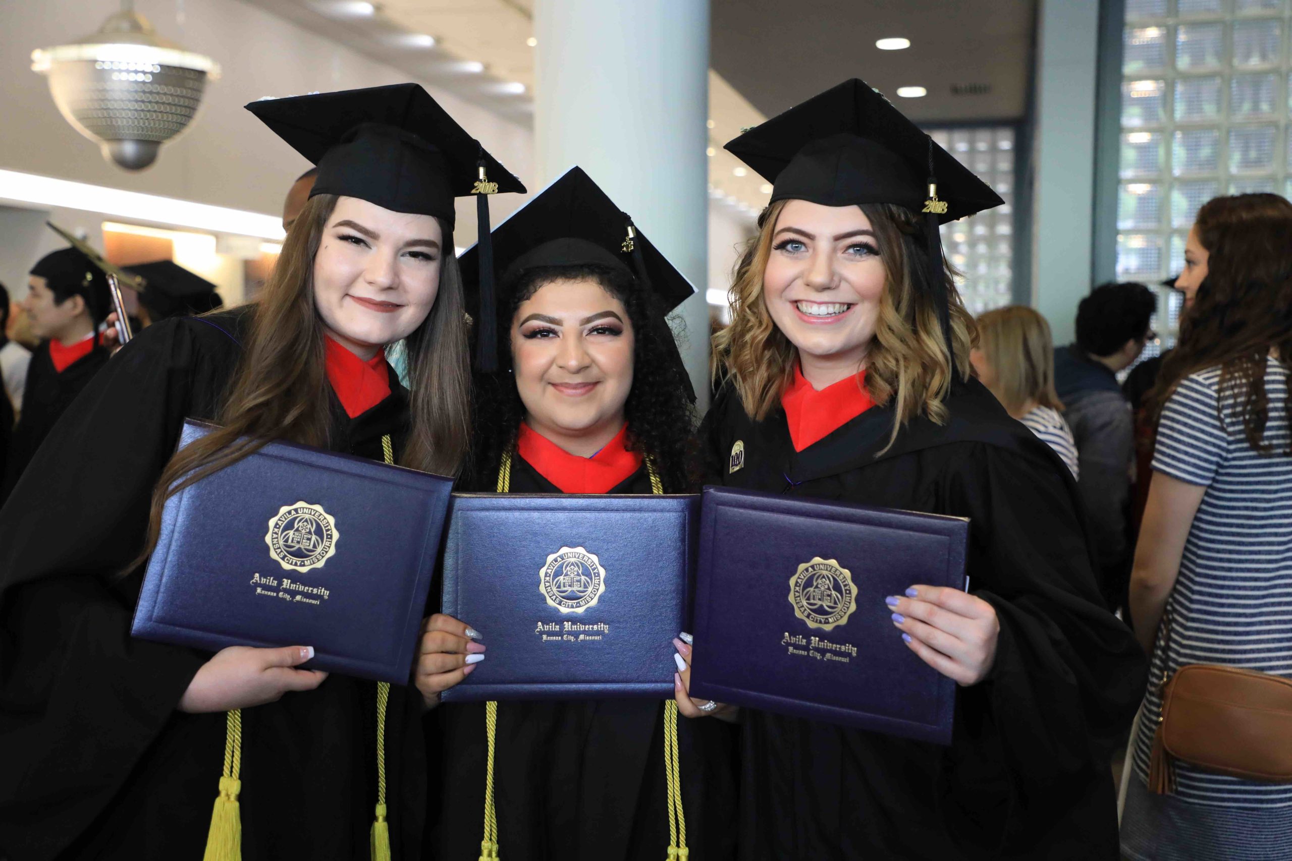 一组三个女人戴着帽子，穿着礼服，在毕业典礼上拿着毕业证摆姿势