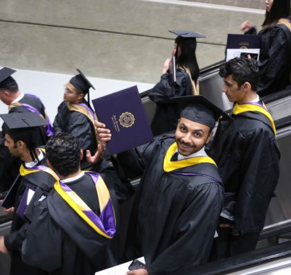 一名毕业生骄傲地拿着他的毕业证书，坐着满是应届毕业生的自动扶梯走下电梯