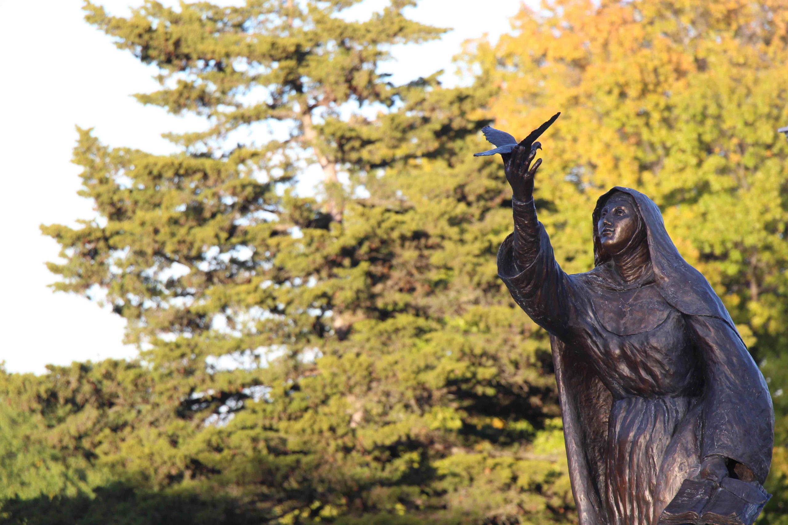 The statue of St. Teresa of Avila with fall foliage in the background.