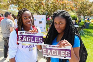 Two students proudly holding up the personalized license plates they created at a campus carnival. Both license plates say "Eagles"