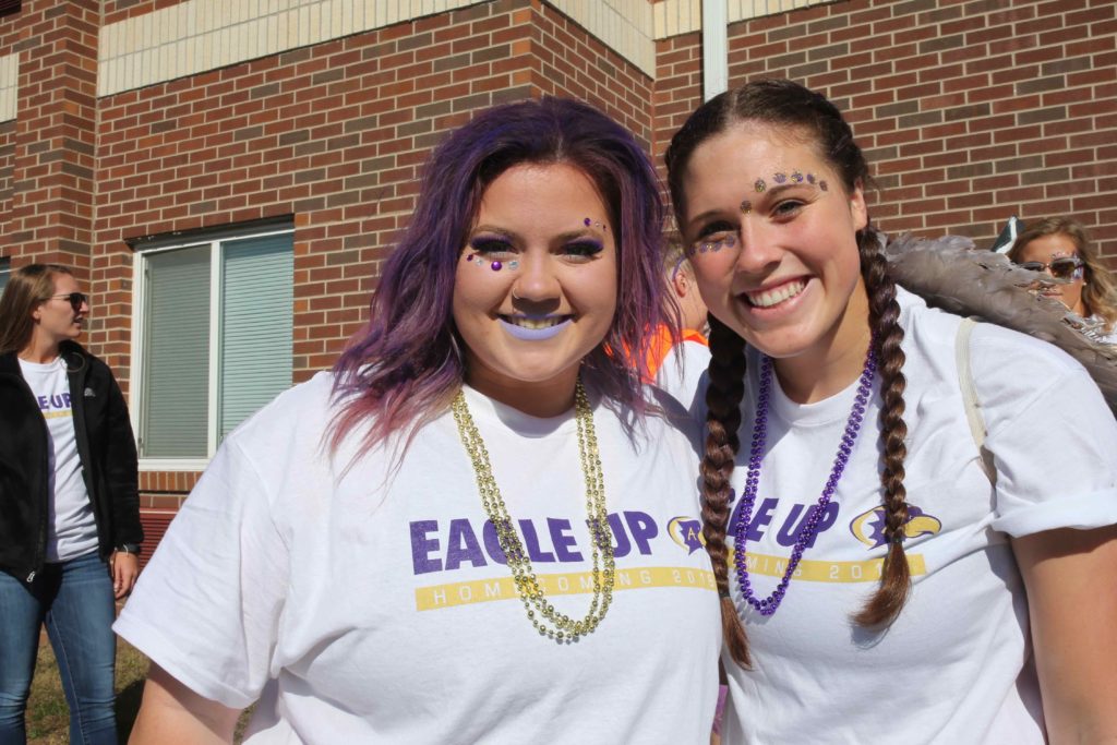 Two students wearing face paint and mardi gras beads pose for the camera during homecoming
