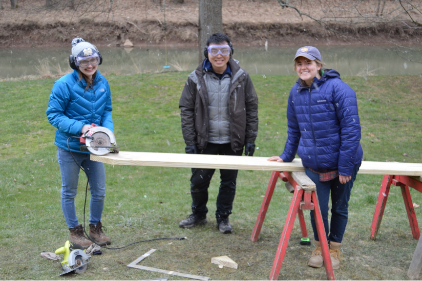 Three students with lumber, saw horses and hand saw