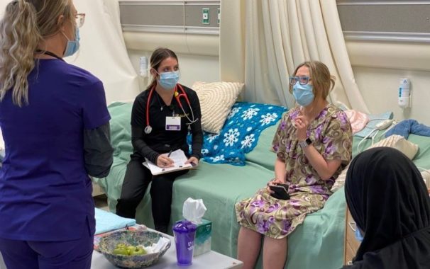 一个社会工作专业的学生(右)看着两个护理专业的学生向“病人”询问她的健康状况.