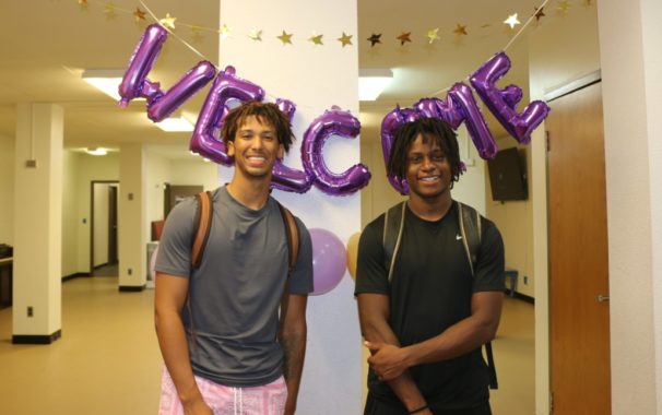 两名阿维拉学生站在一个紫色的欢迎标志前
