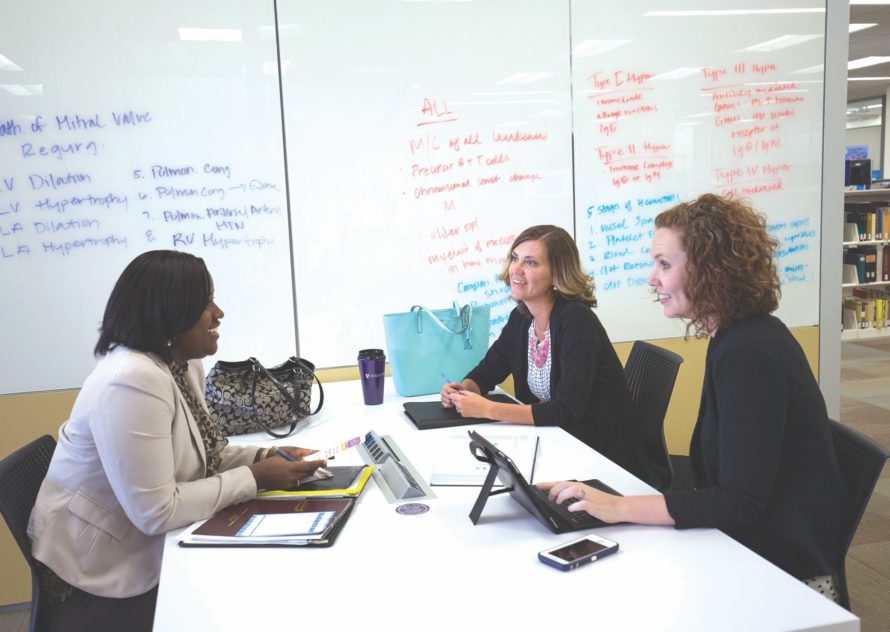 Three adult students talking at a table inside the Leaning Commons