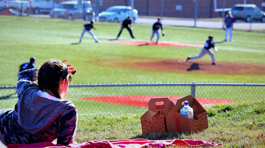 Fan sitting on the hill watching a baseball game