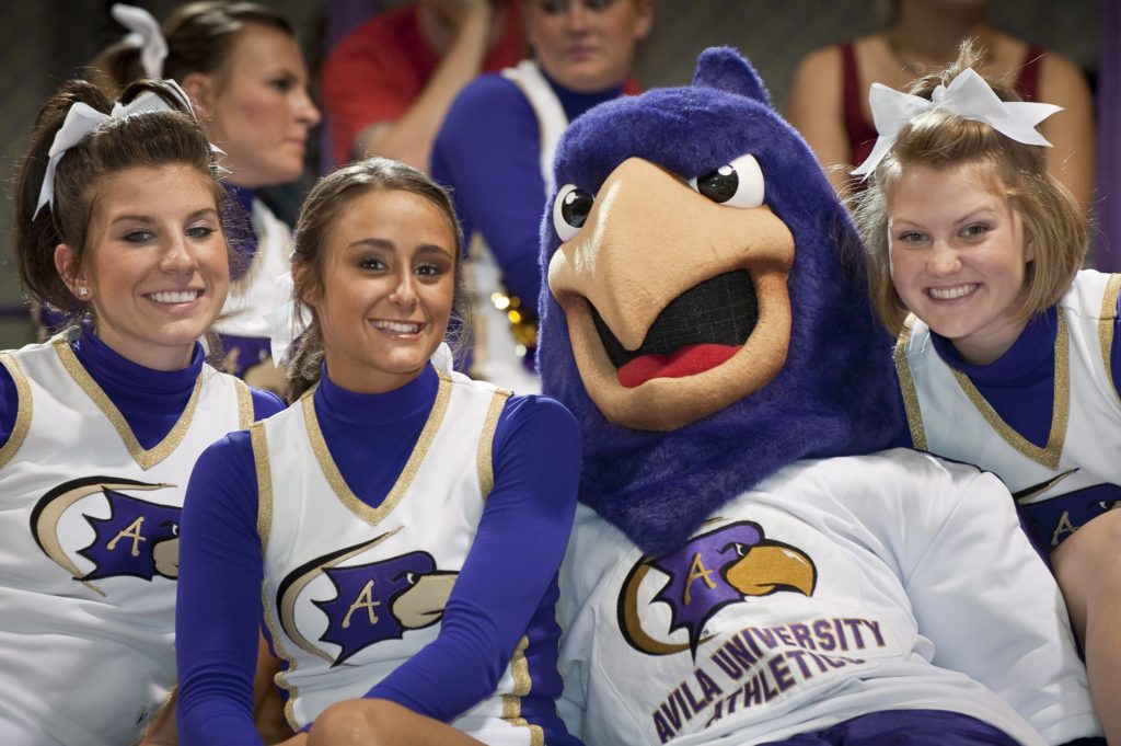Dom the Avila Eagle mascot posing with three cheerleaders