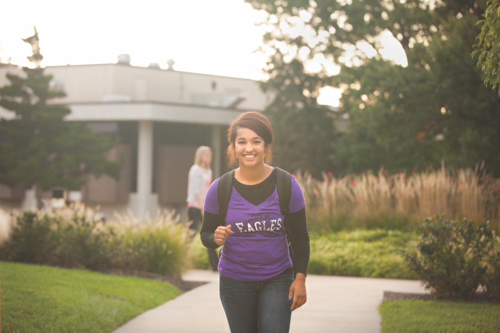 Avila student with backpack walking toward camera on campus
