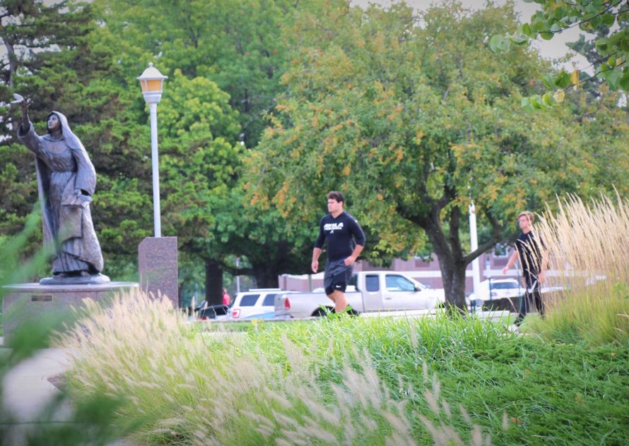 Two students walking toward statue of St. Teresa of Avila