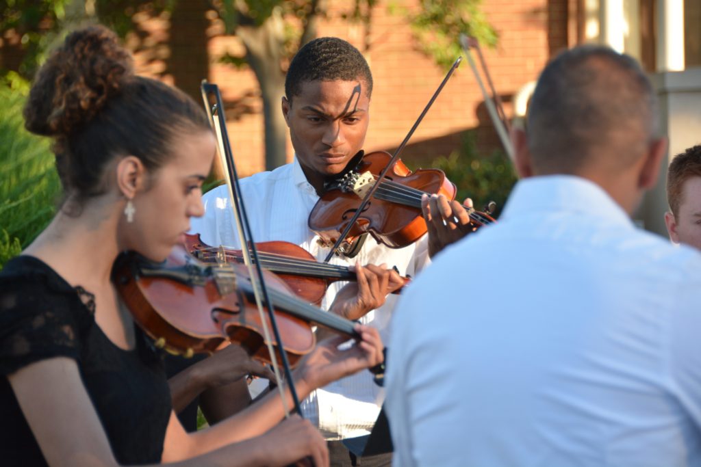 Close up of students playing the violin outside Blasco Hall