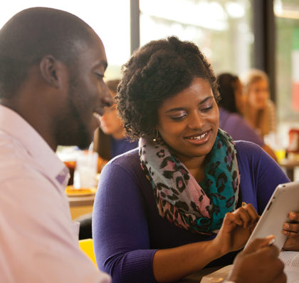 Two adult students sharing an iPad while seated in the dining hall.