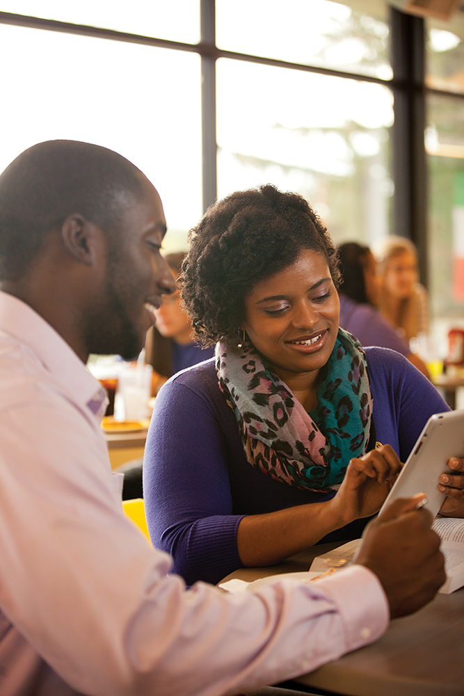 Two adult students sharing an iPad while seated in the dining hall.