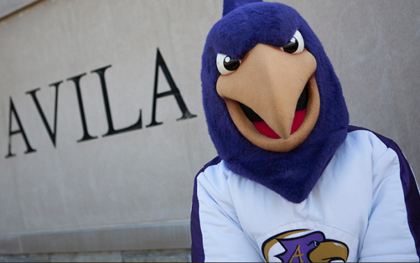 The Avila mascot, Dom the Eagle, standing in front of Avila campus sign