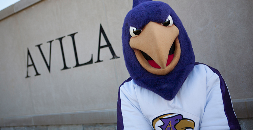 The Avila mascot, Dom the Eagle, standing in front of Avila campus sign