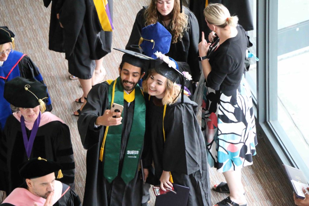 An overhead view of two graduates taking a selfie in their caps and gowns