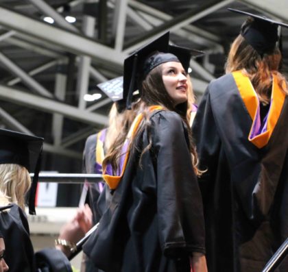 A graduate looks over her shoulder as she walks up the stairs to the commencement stage