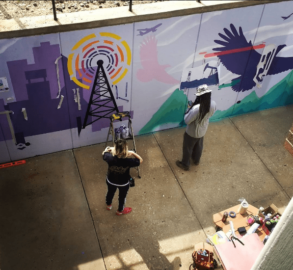 Mural artists painting the mural in the moat surrounding Marian Center
