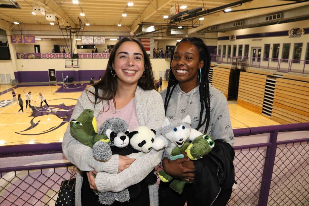 Two students pose with their arms filled with stuffed animals inside Mabee Fieldhouse