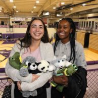 Two students pose with their arms filled with stuffed animals inside Mabee Fieldhouse