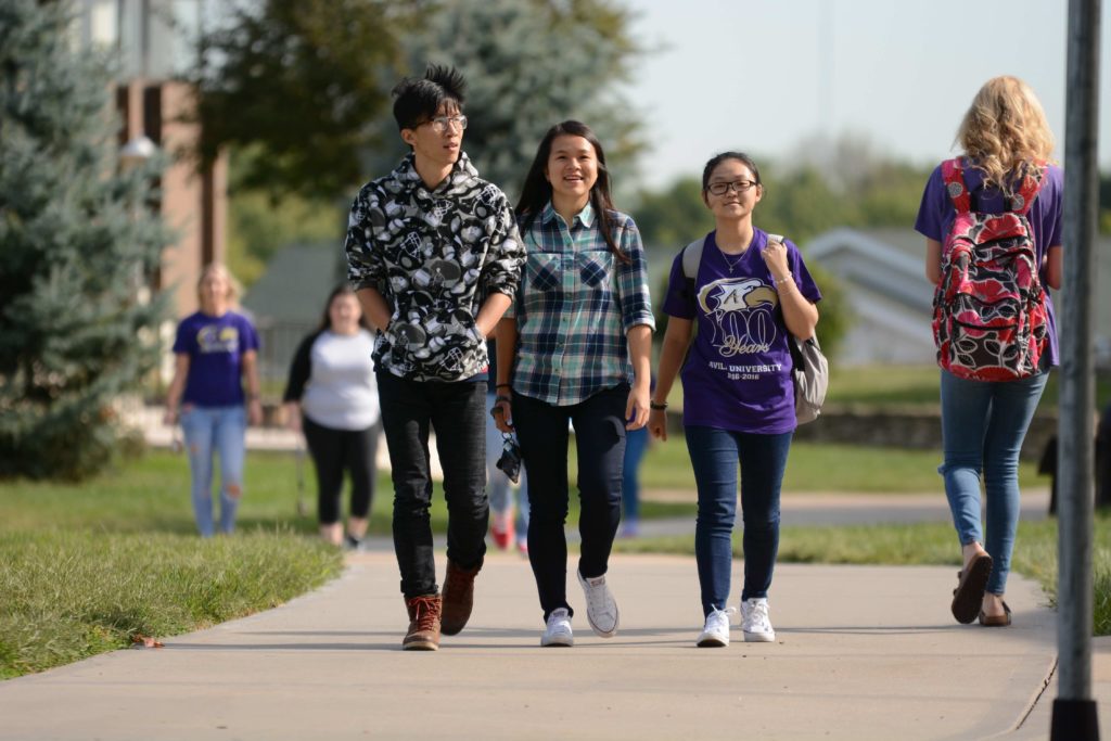 A group of three international students walk along the campus sidewalks