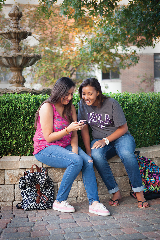 Two students sit on the fountain wall looking at a cell phone