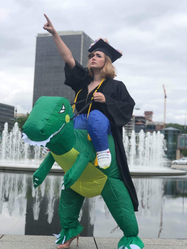 Student in cap and gown wearing a T-Rex costume