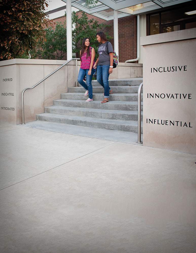 Two students walking down the steps in front of Blasco Hall. Inscriptions on the stairs say, "Inspired. Insightful. Integrated. Inclusive. Innovative. Influential."
