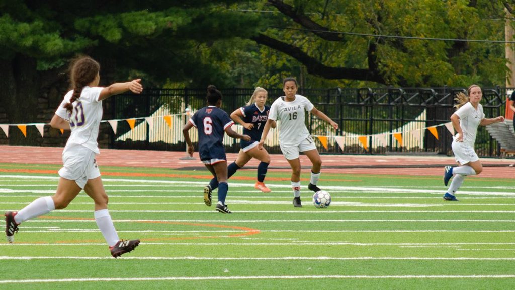 Avila women's soccer player dribbling on the pitch ready to pass to a teammate
