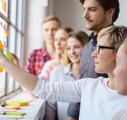 Woman hanging notes on wall in front of group of students