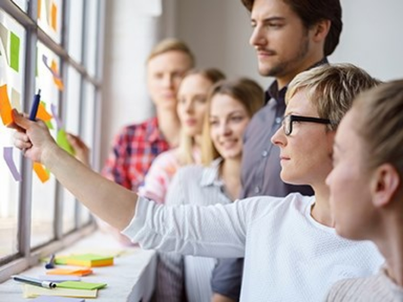 Woman hanging notes on wall in front of group of students