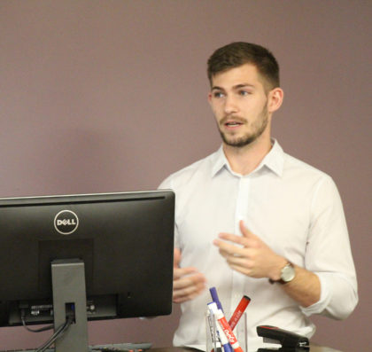 Young man speaking at lectern with computer in foreground