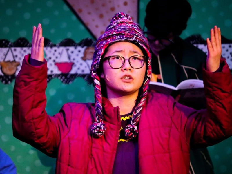 Young woman actor in jacket and hat with hands raised