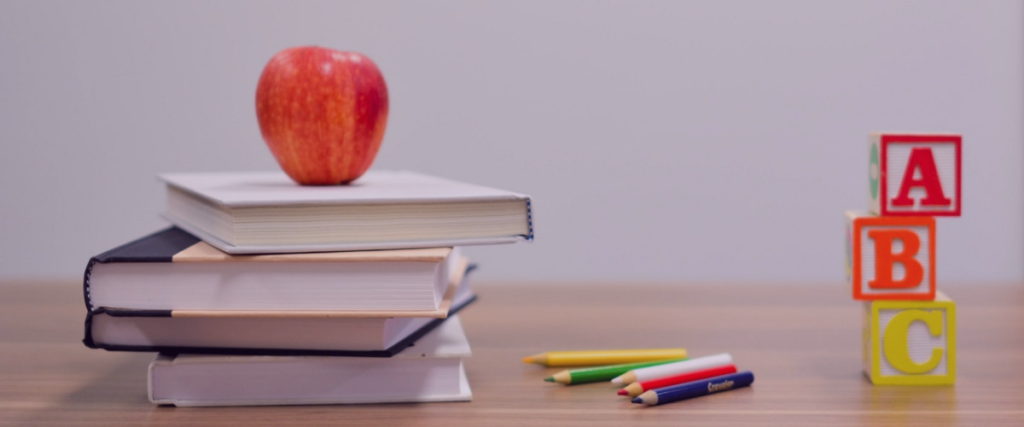 Book with apple on it, colored pencils, and letter blocks on a table