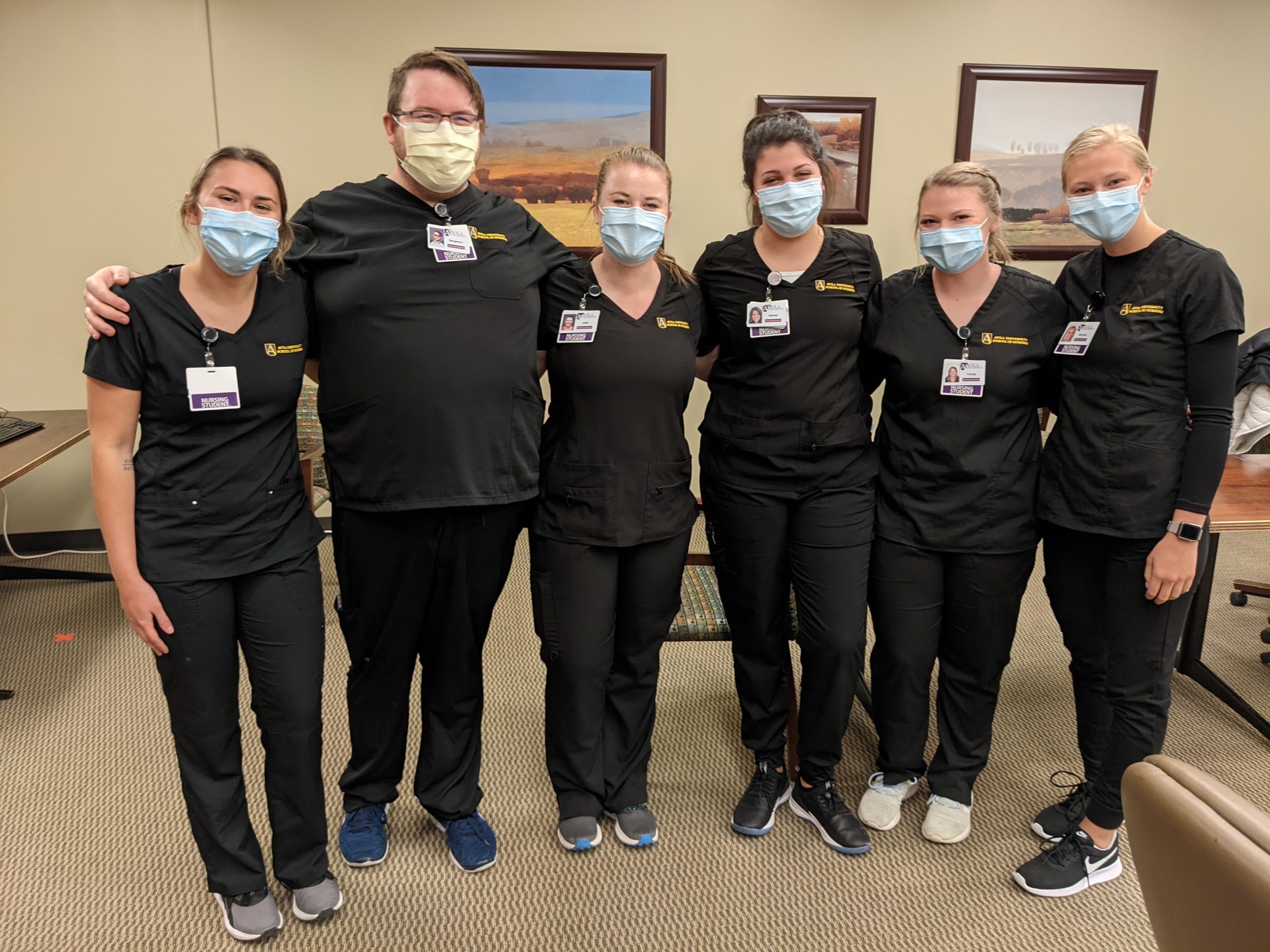 A group of nursing students in scrubs posing in room.