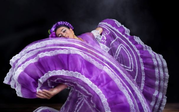 Mexican dancer from the state of Veracruz with a purple dress braid and colorful flowers, happy dancing traditional harp sones with black background and wooden floor C