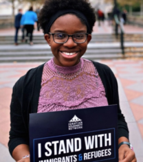 Woman holding a sign, "I stand with immigrants and refugees"