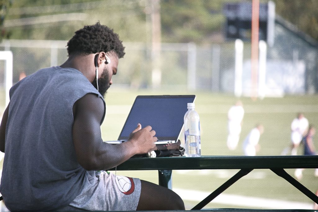 Student studying at a picnic table while soccer match plays out in the background