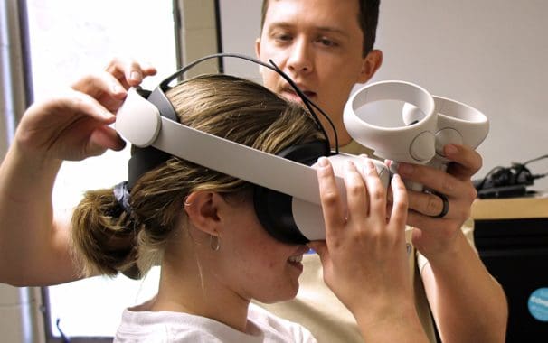 Dr. Jared Branch helps a student adjust a virtual reality headset in the cognitive science lab