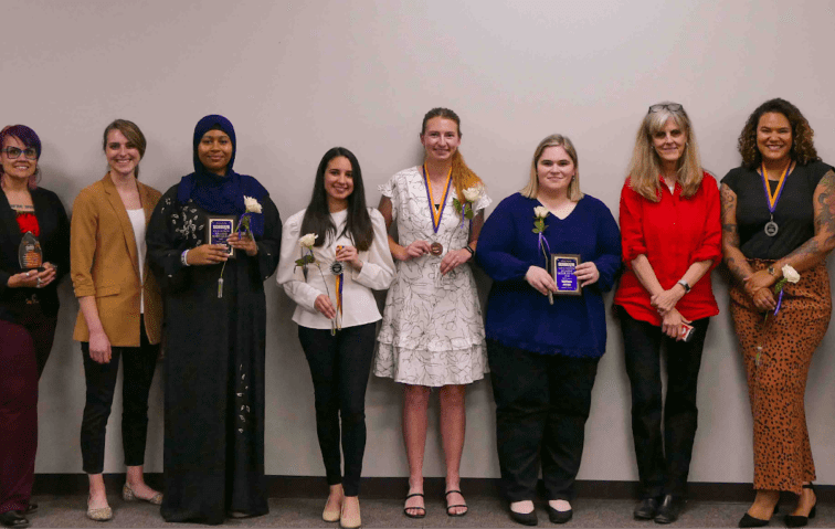 A group of Avila students with their mentors in a row in front of a grey wall