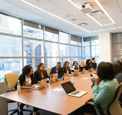 group of people sitting beside rectangular wooden table with laptops
