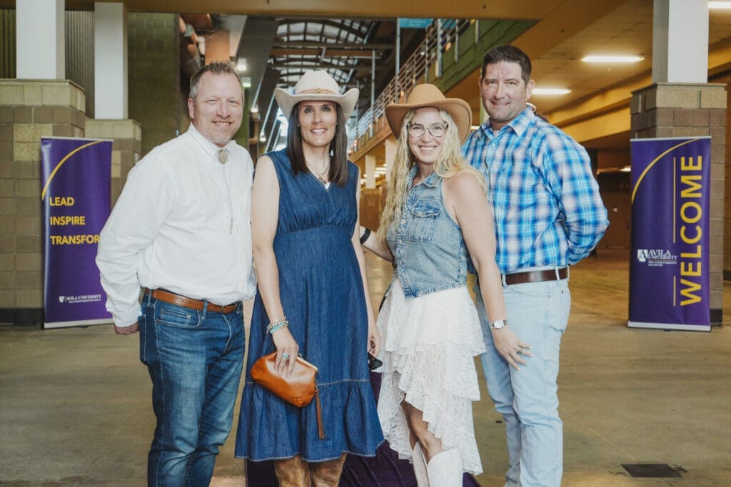 Four guests dressed in formal dark attire pose together and smile at the camera during the Avila University 50th Steer Dinner celebration.