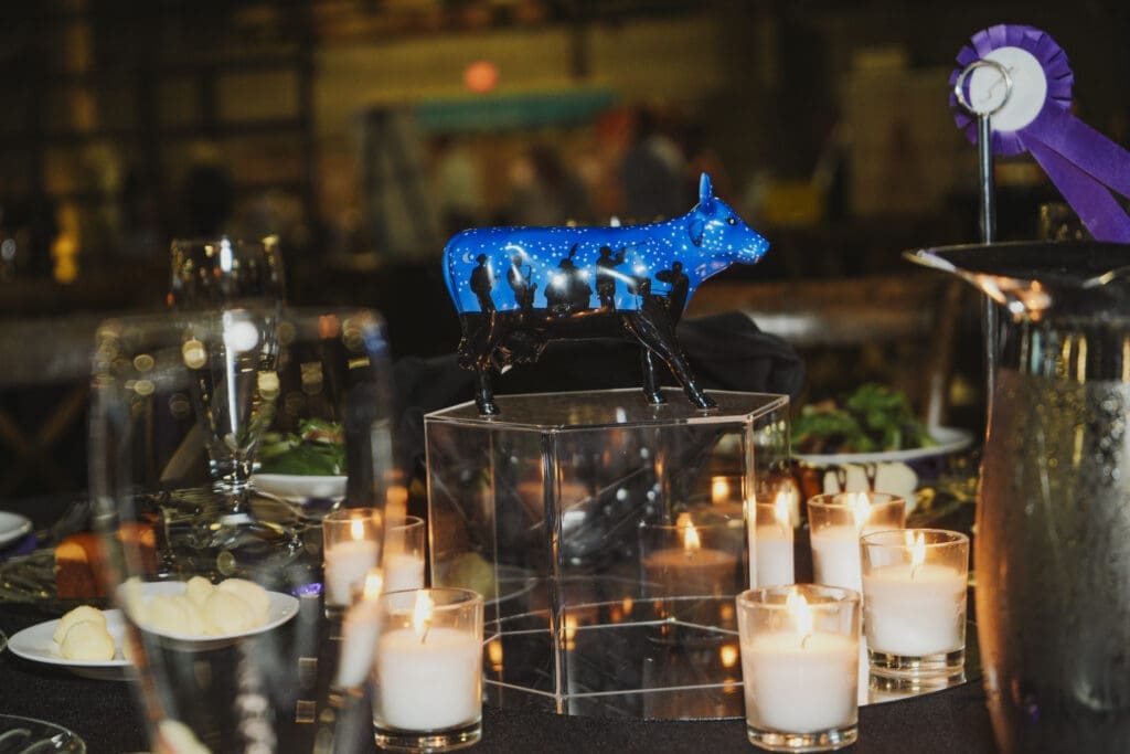 A glowing blue sculptural bull centerpiece is displayed on a lit stage at the Avila University 50th Steer Dinner, with dramatic event lighting and the venue interior visible in the background.