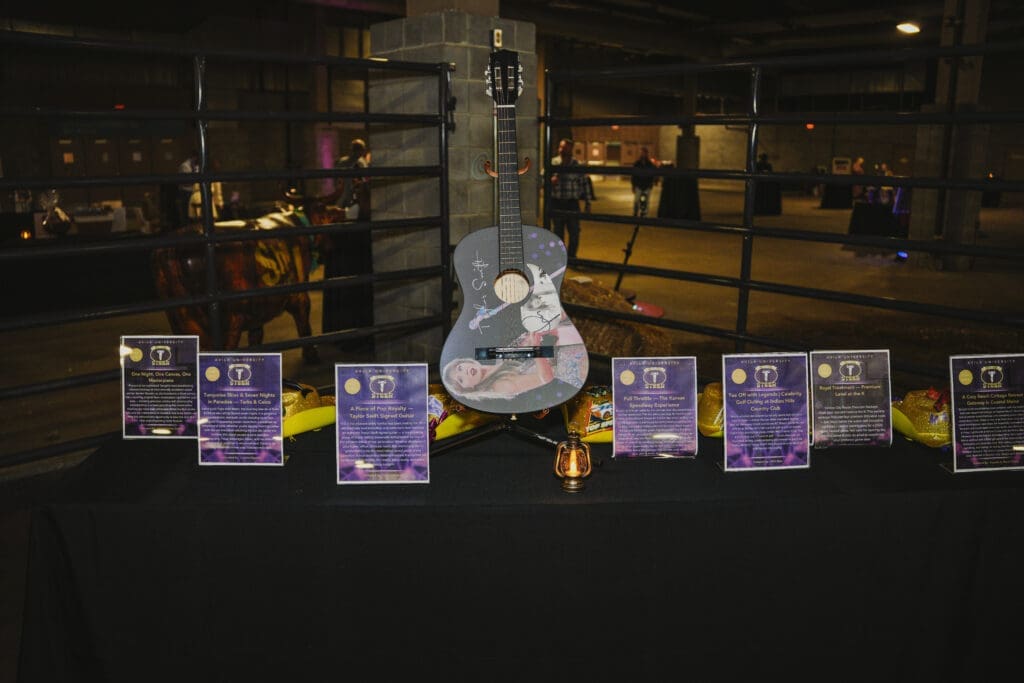 A large indoor event venue decorated in purple and gold lighting for the Avila University 50th Steer Dinner, with round tables set for dinner and guests visible in the background.