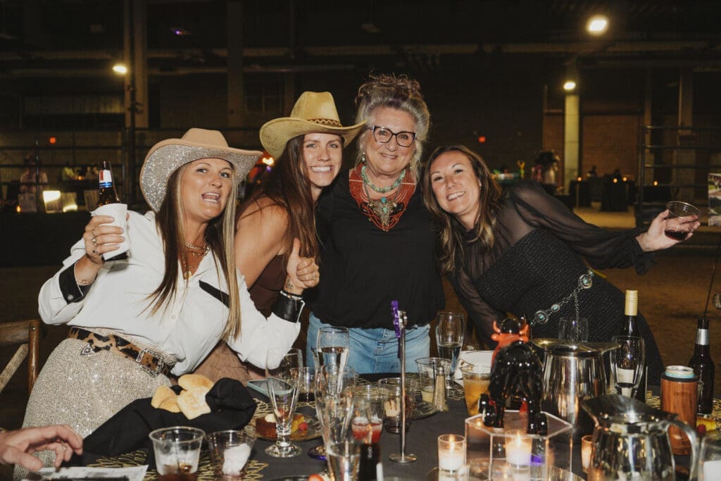 A man in a dark suit poses with two Avila University cheerleaders in blue and gold uniforms at the 50th Steer Dinner gala event.