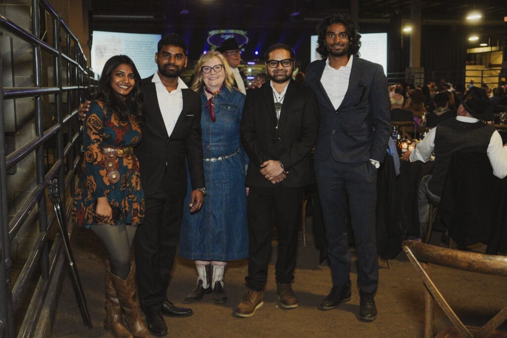 A group of men and women dressed in western-themed attire pose together smiling at the Avila University 50th Steer Dinner, with dinner tables and event décor visible in the background.