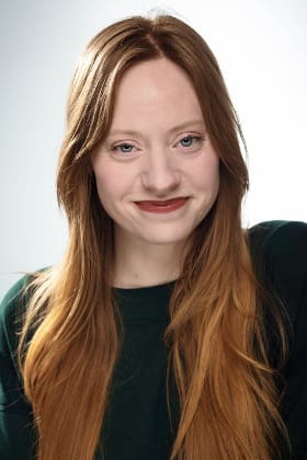 Photograph of a person with long, straight red hair wearing a dark green top against a plain light background. The face is blurred, focusing attention on hair texture and clothing color.