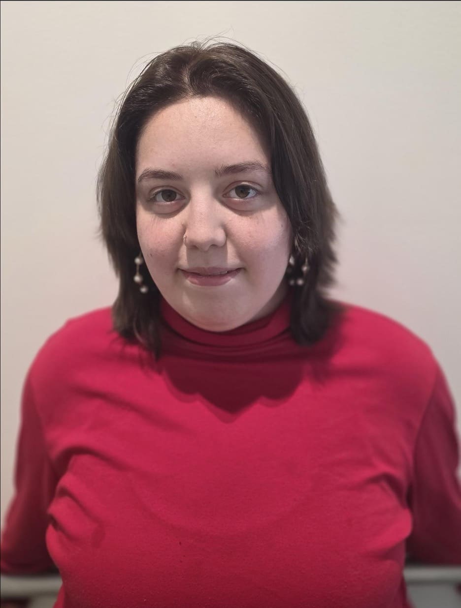 Photograph of a person wearing a red shirt against a plain light-colored background. The person's face is obscured by a blur, focusing attention on the upper body and clothing.