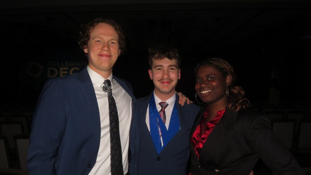 Three Avila University students dressed in professional attire smiling together at a Collegiate DECA event.
