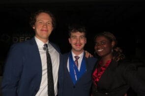Three Avila University students dressed in professional attire smiling together at a Collegiate DECA event.